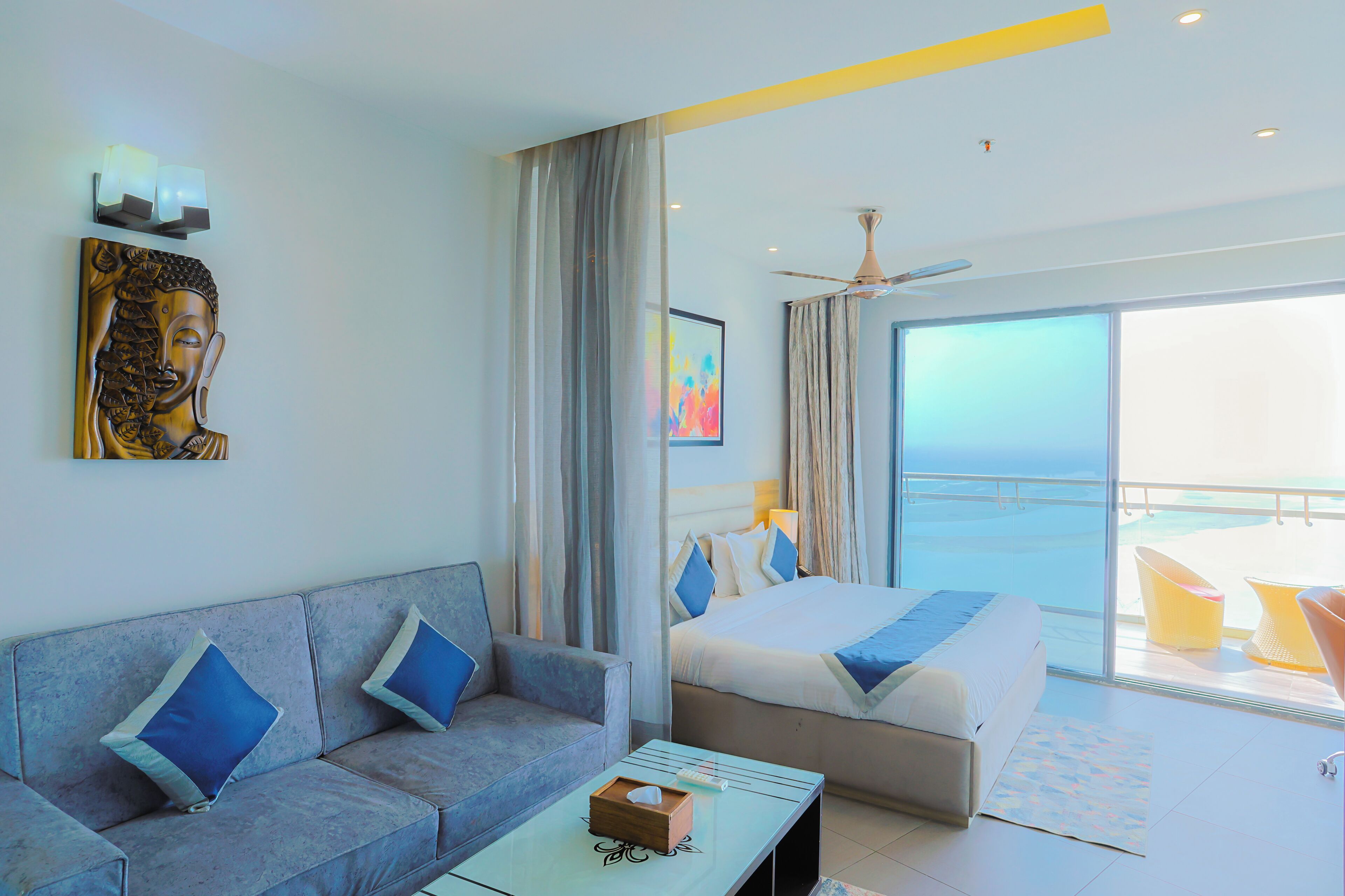 A modern hotel room with a sofa, a bed, and a balcony with a view of the sea.