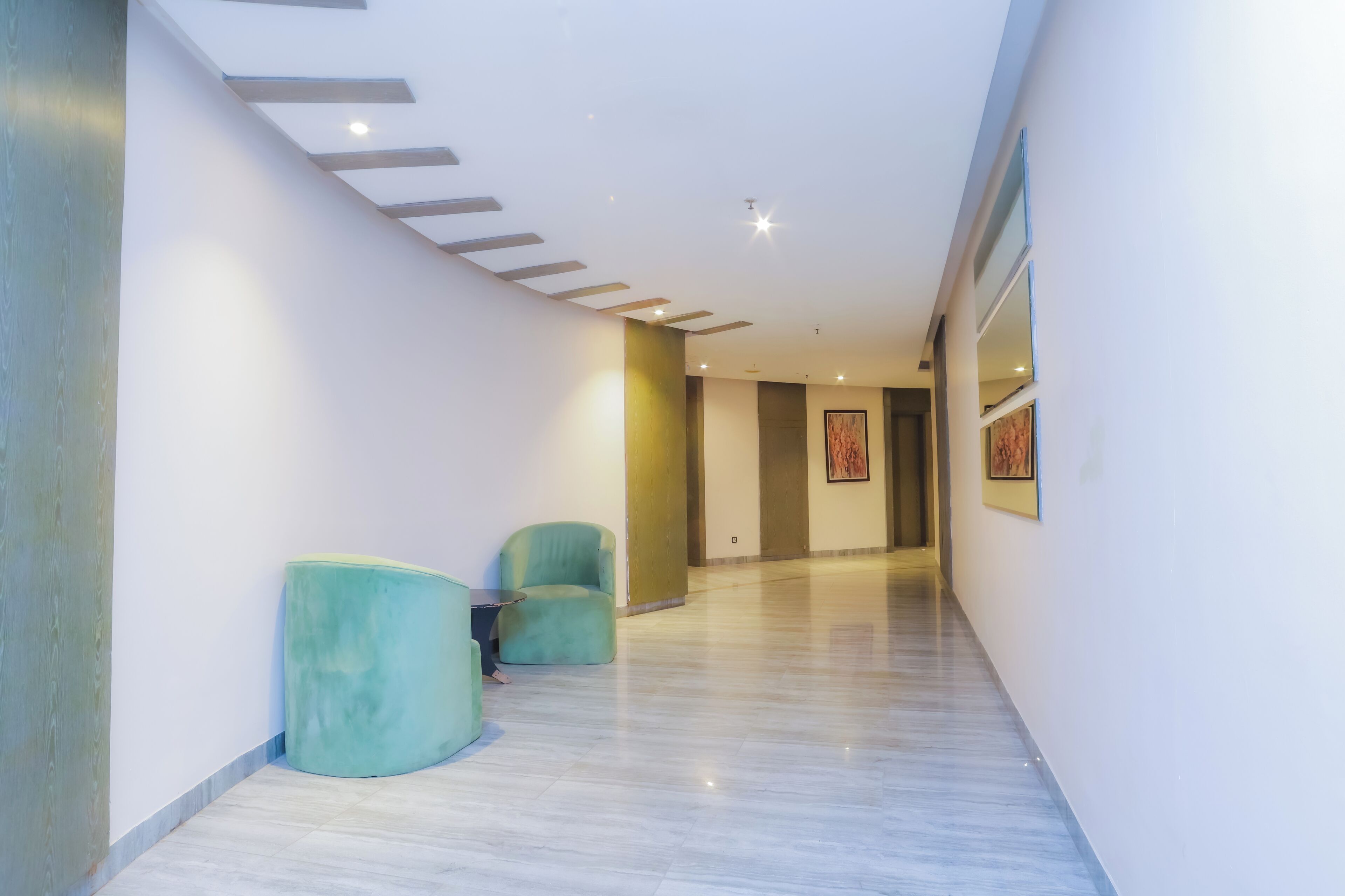 A modern hallway with a marble floor, two teal chairs, and a small table.