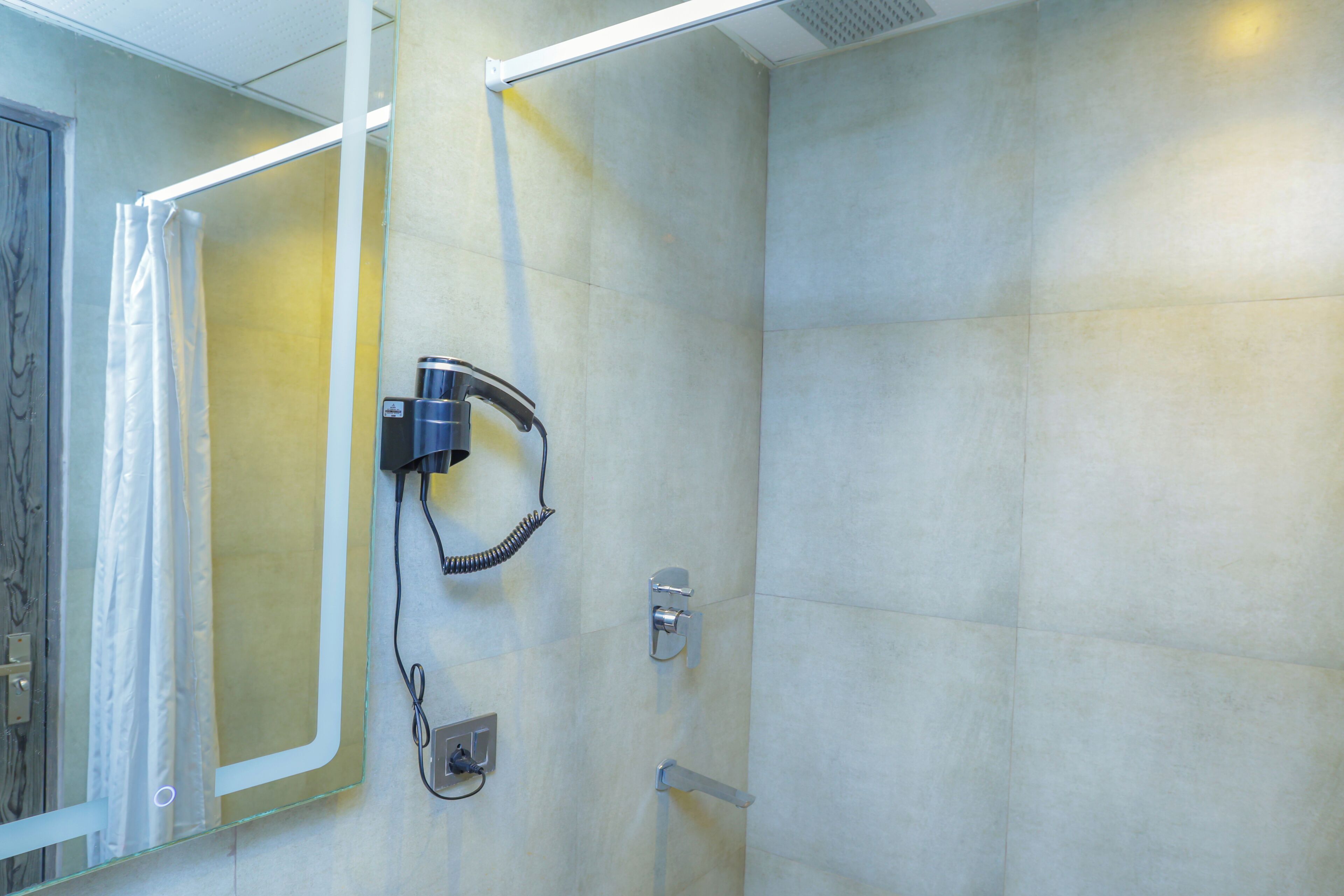 Casa de banho com cabine de chuveiro em vidro, secador de cabelo fixado na parede e porta-toalhas.