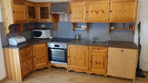 A compact kitchen with wooden cabinets, a microwave, an oven, and a sink. - Cësa Giulio - near the Sellaronda ski area / Dolomites (Campitello di Fassa)
