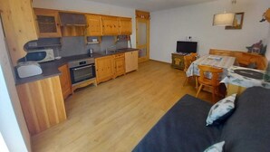 A compact kitchen with wooden cabinets, a microwave, and a sink. There is a dining area with a table and chairs, and a sofa with cushions. - Cësa Giulio - near the Sellaronda ski area / Dolomites (Campitello di Fassa)