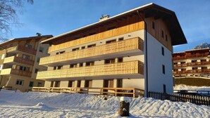 A multi-story hotel with wooden balconies, a snow-covered ground, and a mountainous backdrop. - Cësa Giulio - near the Sellaronda ski area / Dolomites (Campitello di Fassa)