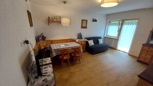 A spacious living area with a wooden dining table, chairs, a sofa, and a small kitchen area with a counter and cabinets. - Cësa Giulio - near the Sellaronda ski area / Dolomites (Campitello di Fassa)