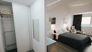 A modern hotel room with a bed, bedside table, chair, and a walk-in closet with a hanging rack. - Cozy Seaside Studio Apartment C - Faraway (Lagoa)