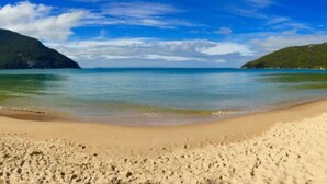Una playa con agua azul cristalina, orilla de arena y colinas verdes al fondo.