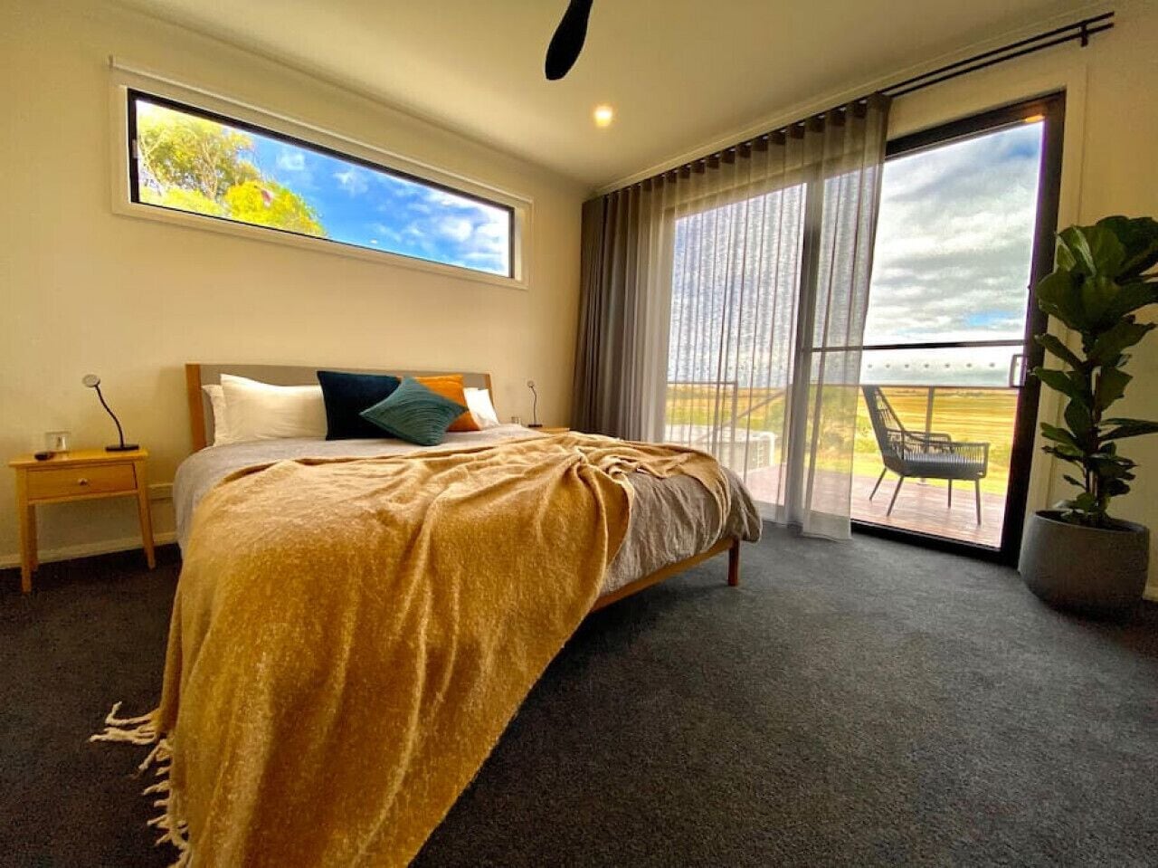 A bedroom with a bed, a nightstand, a large window, and a view of the outdoors.