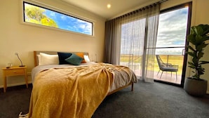 Une chambre à coucher avec un lit, une table de chevet, une grande fenêtre et une vue sur l’extérieur.