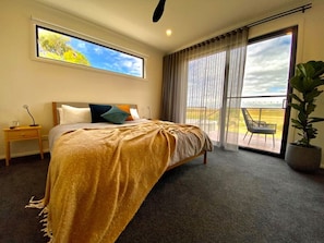 A bedroom with a bed, a nightstand, a large window, and a view of the outdoors.