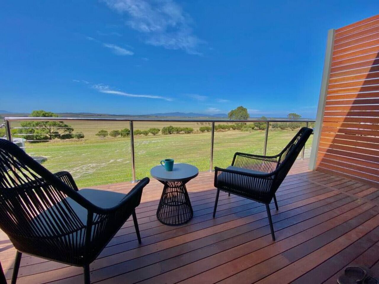 A deck with two chairs and a small table, overlooking a grassy landscape.
