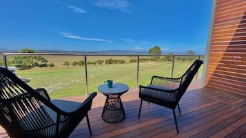 A deck with two chairs and a small table, overlooking a grassy landscape.