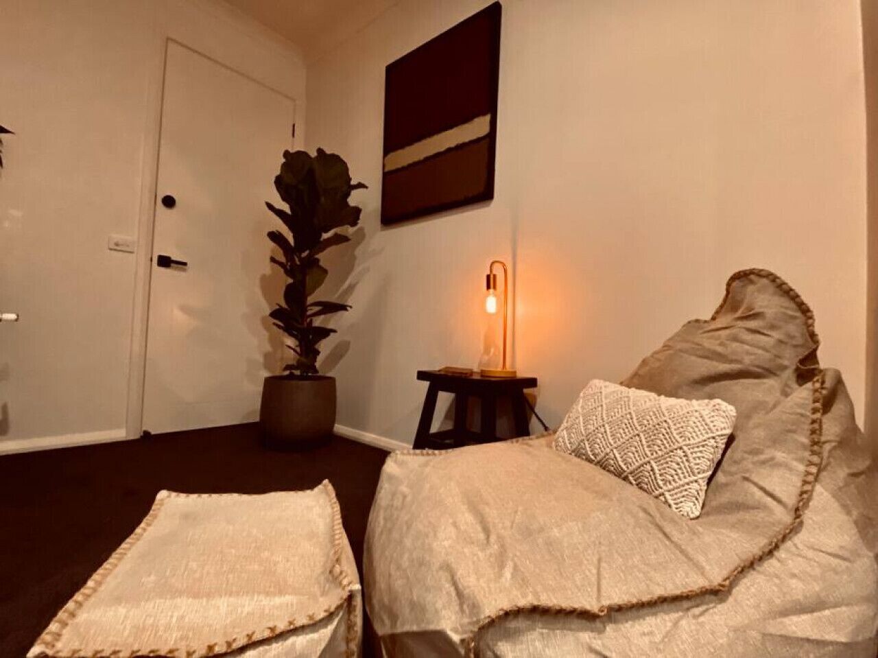 A room with a bed, a bedside table with a lamp, a potted plant, and a door.