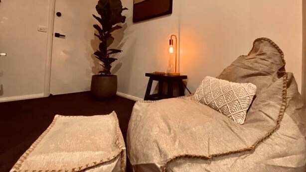 Une pièce avec un lit, une table de chevet avec une lampe, une plante en pot et une porte.