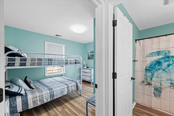 A room with a bunk bed, a desk, a chair, a window with blinds, and a door with a curtain.