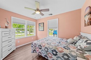 A bedroom with a bed, dresser, windows, and a ceiling fan.