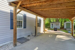 A covered patio area with a concrete floor, wooden beams, and a small shed in the background.