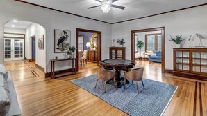 Ein geräumiges Wohnzimmer mit Holzböden, einem runden Esstisch mit Stühlen, einem Deckenventilator und einem großen Fenster.