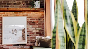Una habitación acogedora con pared de ladrillo, un cuadro enmarcado, una planta y un banco acolchado.