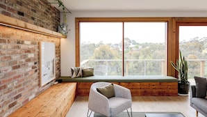 Una habitación moderna con pared de ladrillo, suelo de madera, un ventanal con vistas, un banco y una silla.