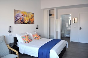A hotel room with a bed, a chair, a painting, a wardrobe, and a bathroom visible through an open door.