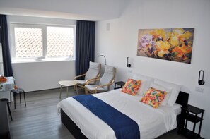 A hotel room with a bed, a chair, a desk, and a window with curtains.