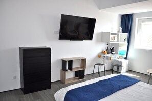 A modern hotel room with a bed, a TV, a wardrobe, a desk, and a chair.