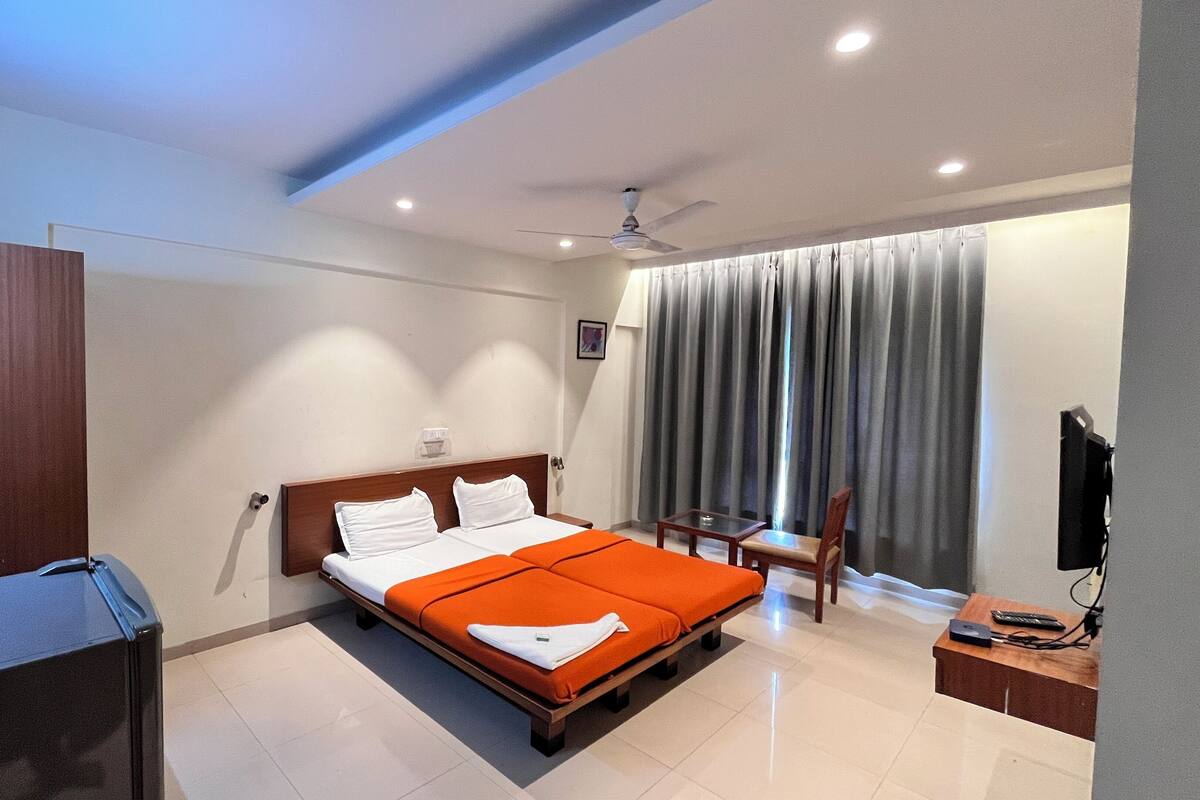 A hotel room with a bed, a desk, a chair, a TV, and a window with curtains.