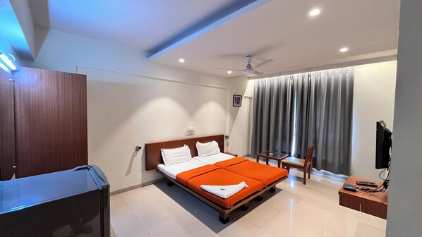 Una habitación de hotel con cama, escritorio, silla, televisor y ventana con cortinas.