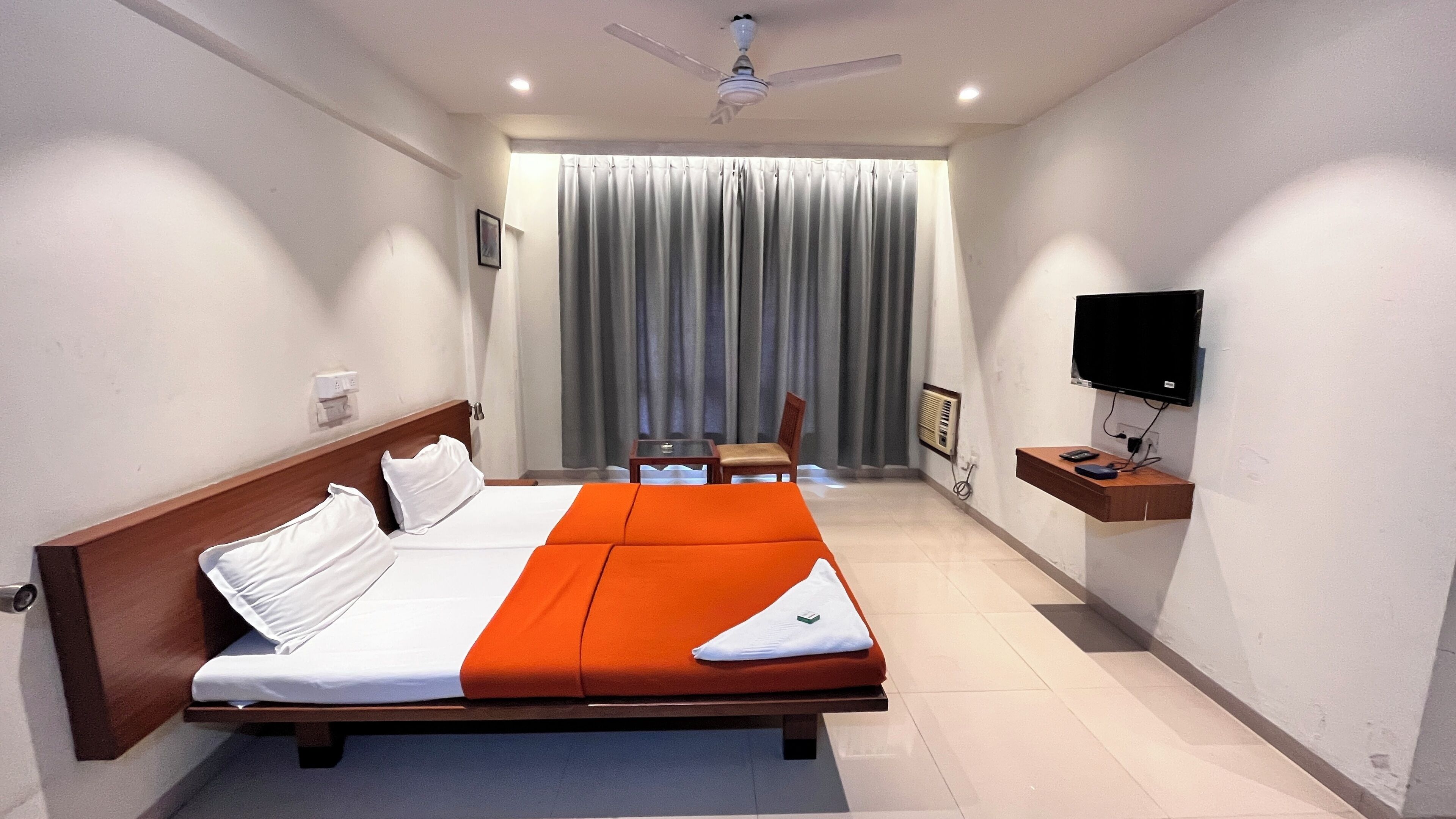 A hotel room with a bed, a desk, a chair, a television, and a window with curtains.