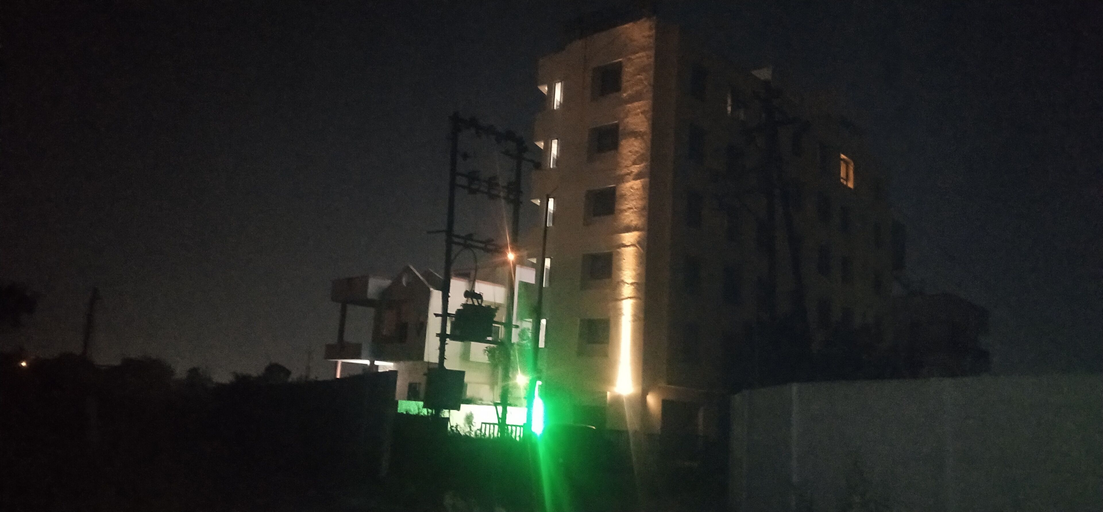 Vista nocturna de un edificio de varios pisos con ventanas iluminadas y un semáforo en verde.