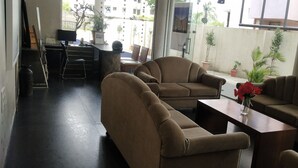 A modern lounge area with sofas and a coffee table, a desk with a computer, and potted plants. - Hotel Sumanchandra Suites  (Nashik)
