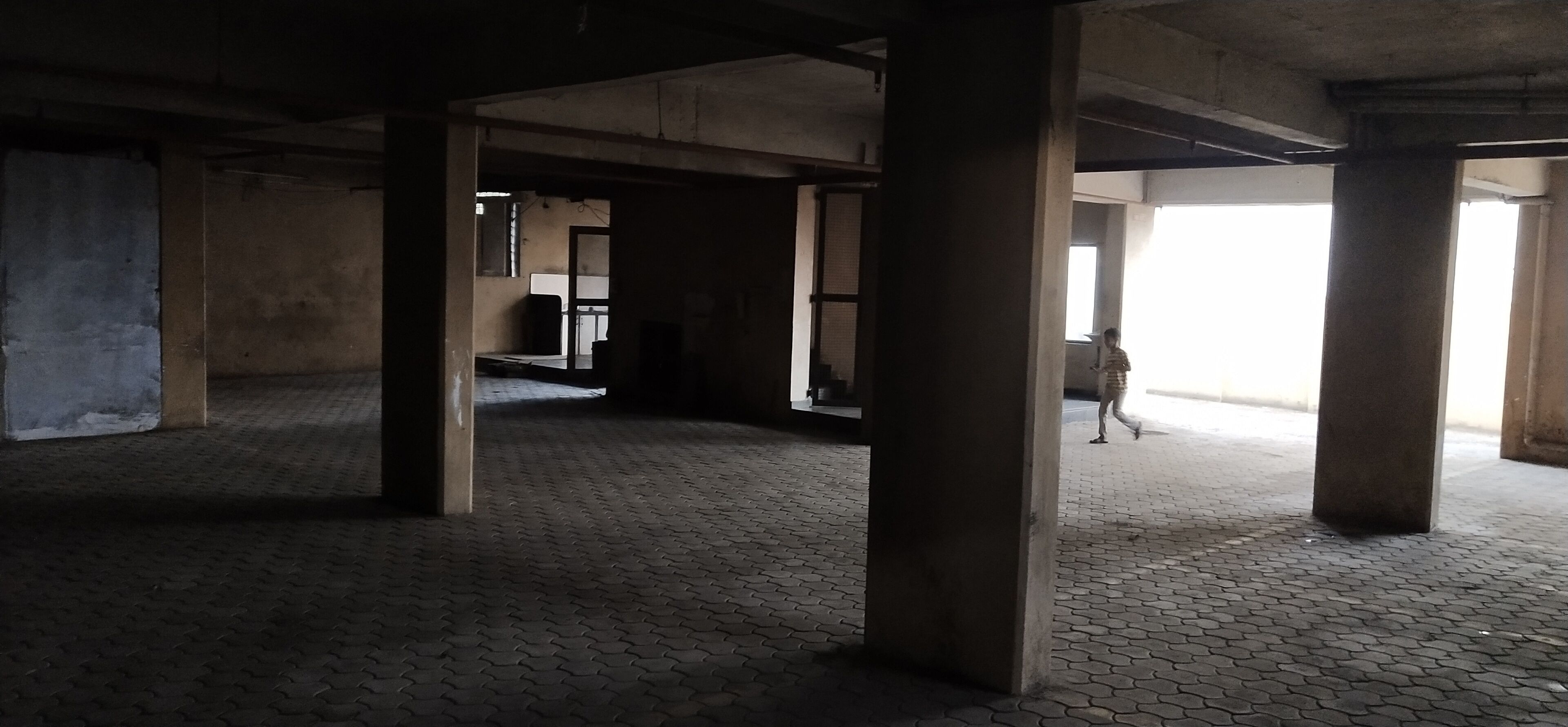 An interior space with concrete pillars, a tiled floor, and a person walking.