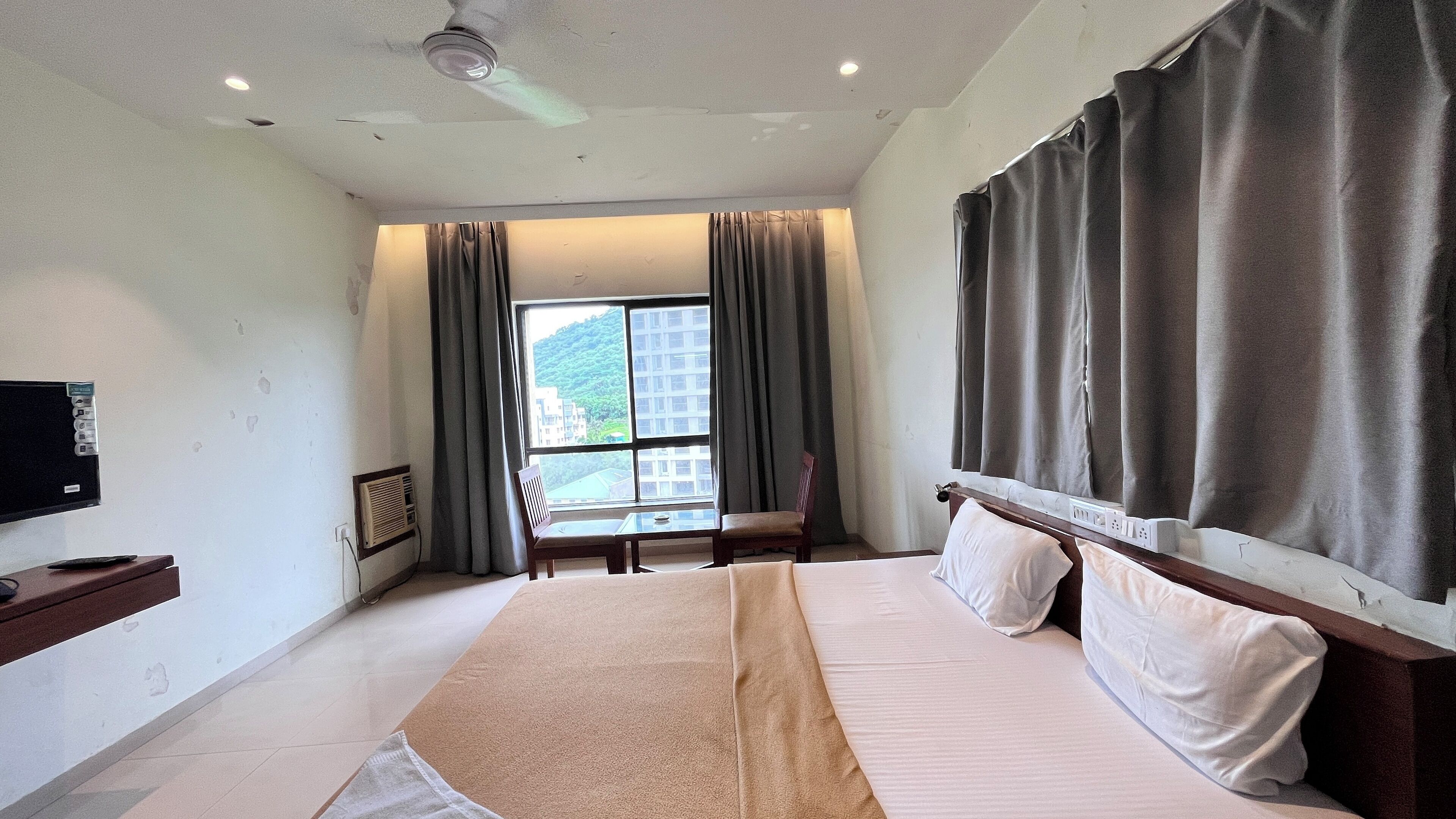 A hotel room with a bed, a TV, a desk, and a window with curtains.