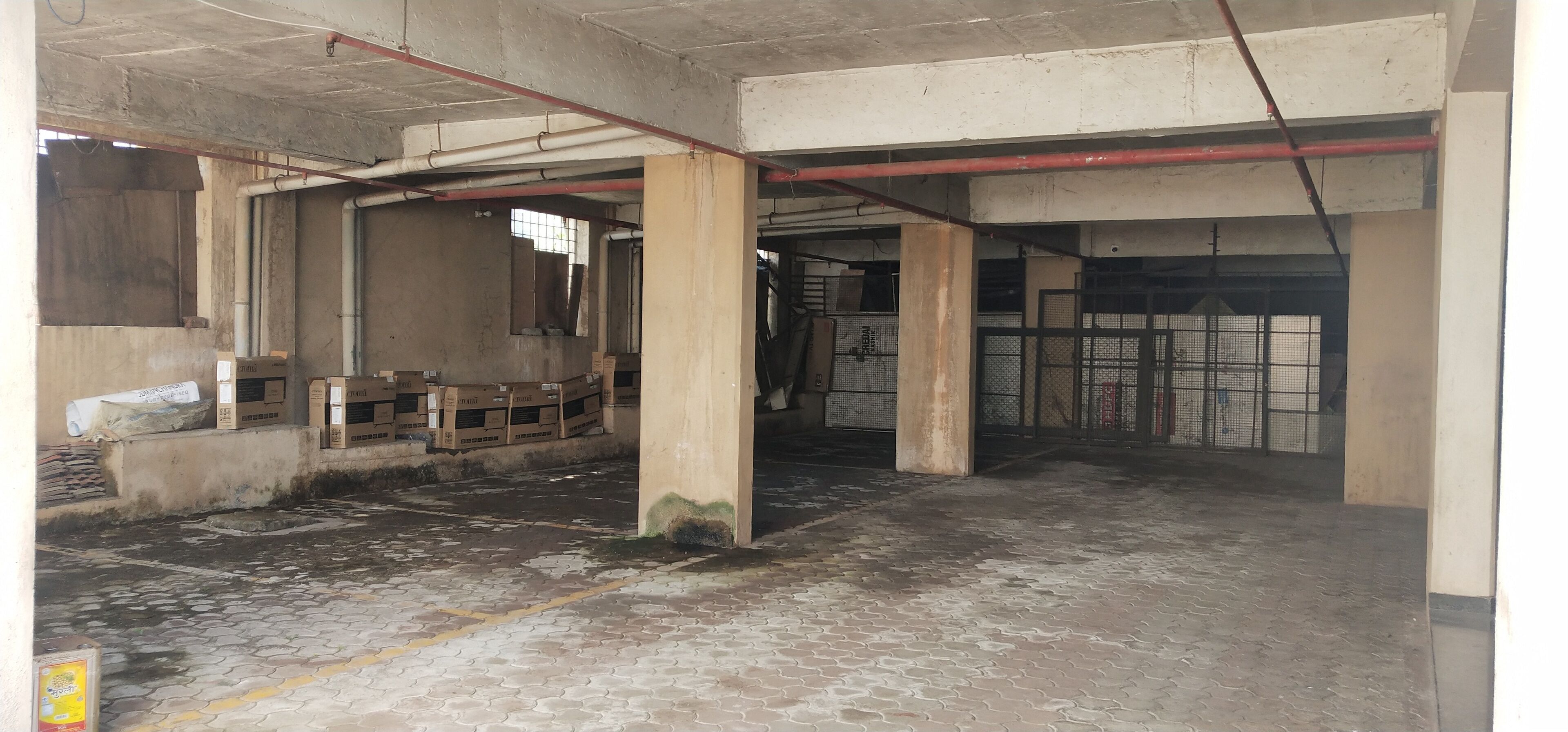 An unfinished interior with exposed concrete pillars, a tiled floor, and scattered cardboard boxes.