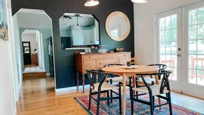 Un comedor con una mesa redonda y sillas, una cocina con un espejo grande, y vistas a través de una puerta.