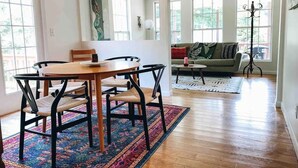 Un amplio salón con una mesa y sillas de madera, una alfombra colorida y un sofá con cojines.