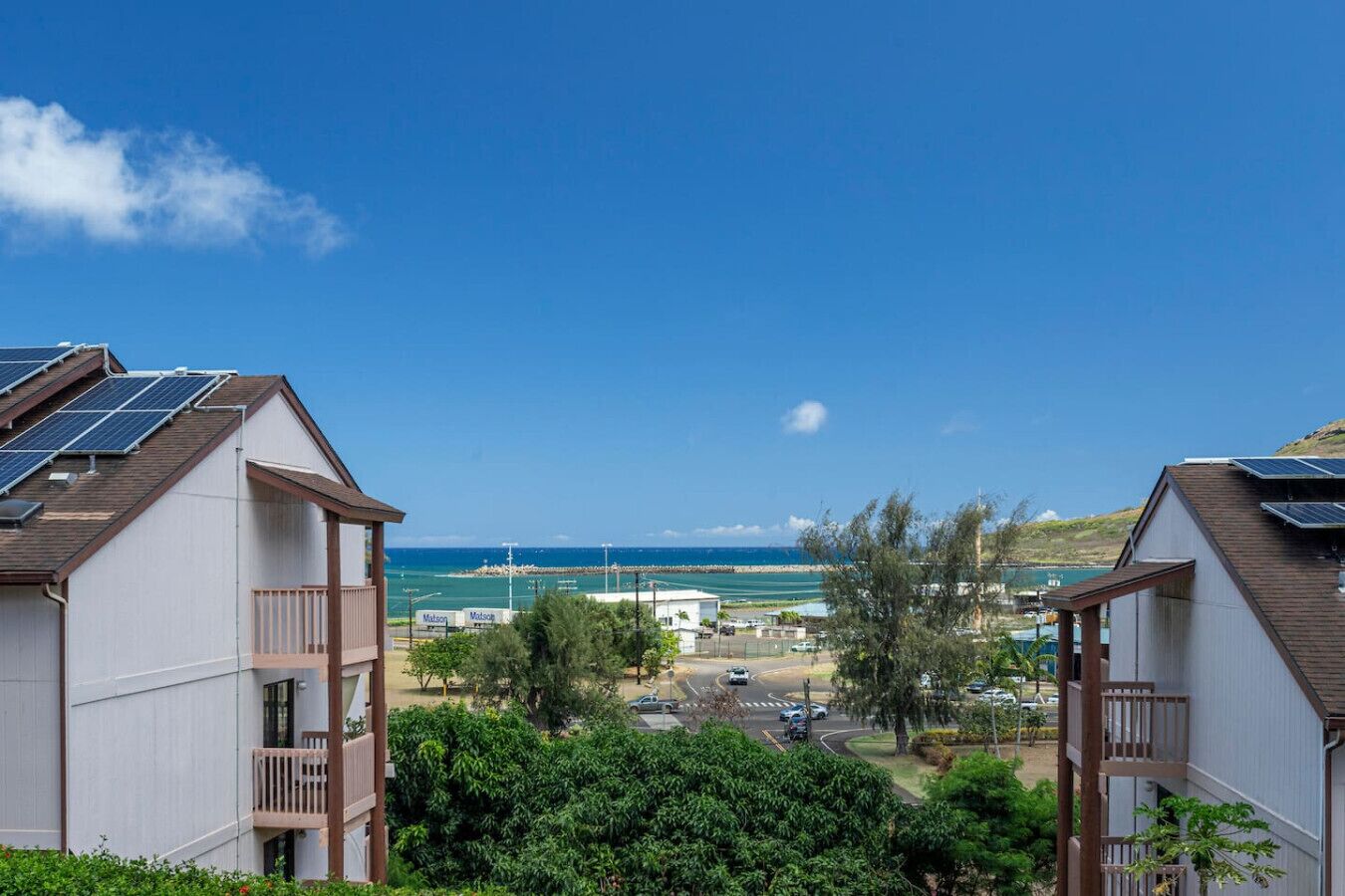 Zona residencial amb dues cases, cadascuna amb panells solars a la teulada, vista al mar i un cel serè.