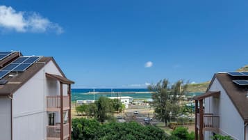 Zona residencial amb dues cases, cadascuna amb panells solars a la teulada, vista al mar i un cel serè.