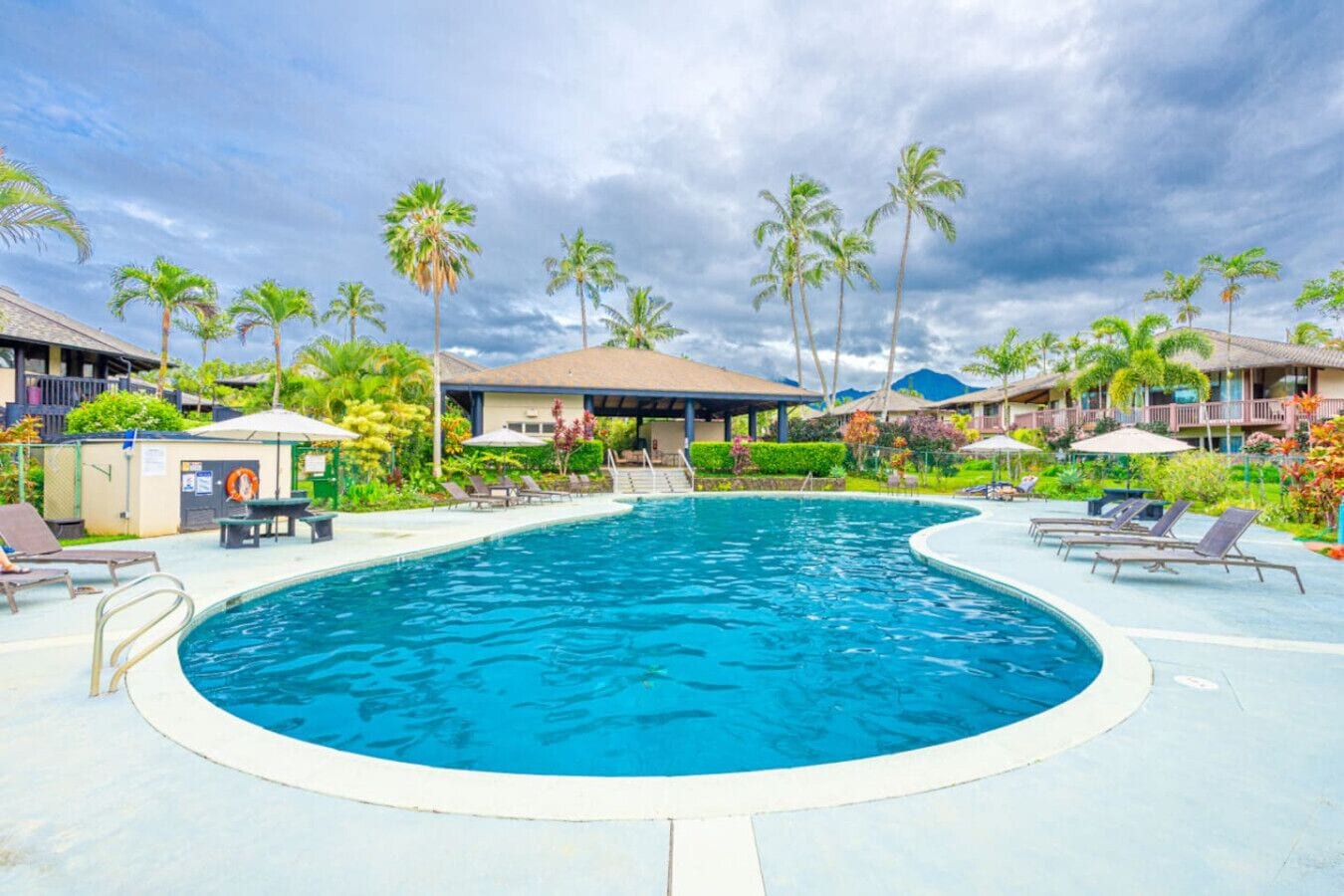 A swimming pool with lounge chairs, palm trees, and resort buildings.