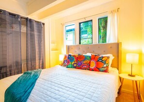 A bedroom with a bed, curtains, a window, and a bedside lamp.