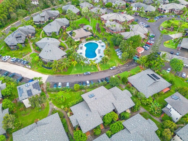 Une vue aérienne d’un quartier résidentiel comprenant plusieurs maisons, une piscine centrale et une route.