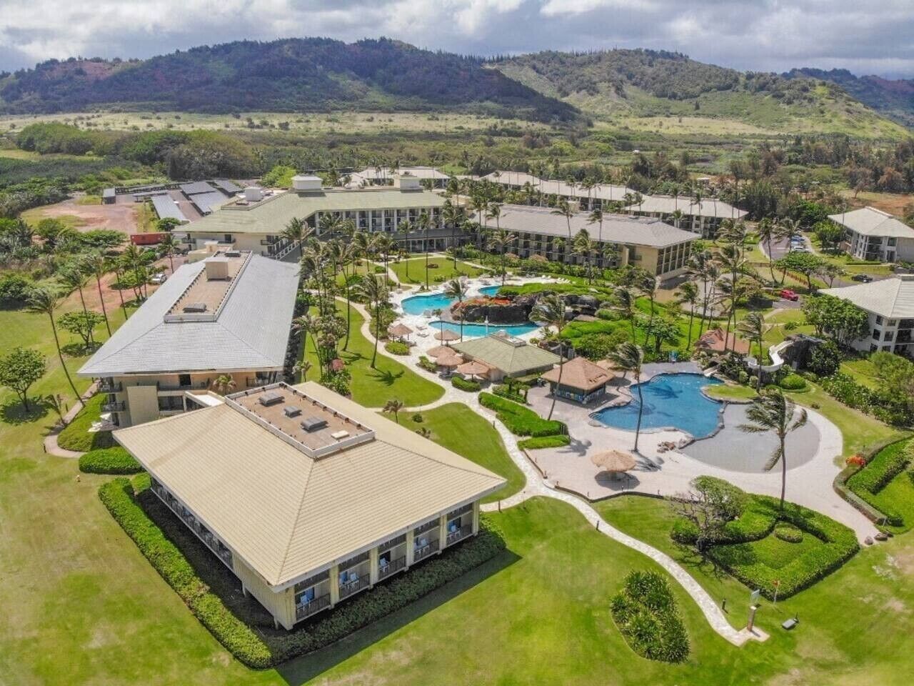 Um resort com vários edifícios, uma área de piscina central e jardins paisagísticos ao redor.