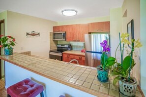 A kitchen with wooden cabinets, a microwave, a refrigerator, and a sink. There are potted plants on the counter.
