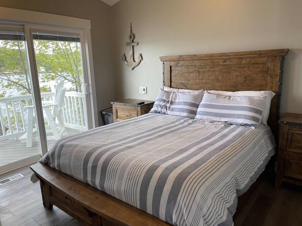 Un dormitorio con una cama grande, cabecera de madera y un banco al pie de la cama. Se ve una ventana con vistas a una terraza y árboles.
