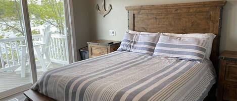Un dormitorio con una cama grande, cabecera de madera y un banco al pie de la cama. Se ve una ventana con vistas a una terraza y árboles.