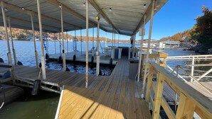 A wooden dock with a covered walkway, boats docked in the background, and a clear view of the water. - Luxury Main Channel Lake House, Dock, Party Bar (Rocky Mount)