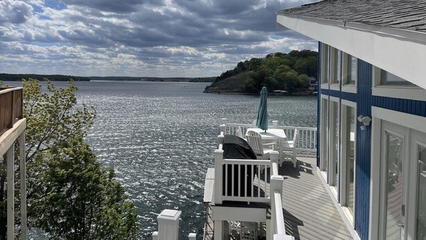 A waterfront property with a deck overlooking a body of water, a view of a distant island, and a building with large windows. - Luxury Main Channel Lake House, Dock, Party Bar (Rocky Mount)
