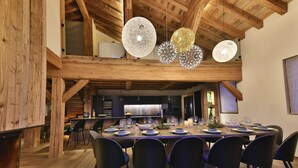 A dining area with a high ceiling, wooden beams, and modern pendant lighting.