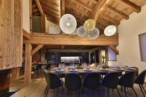 Un espace repas doté d’un plafond haut, de poutres en bois et d’un éclairage moderne suspendu.
