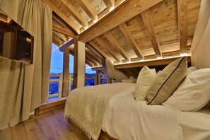 Un dormitorio acogedor con techo de madera, una cama grande con ropa blanca y vistas a un paisaje nevado a través de una ventana.