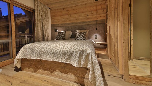 A wooden bedroom with a bed, a nightstand, and a view of the outside.